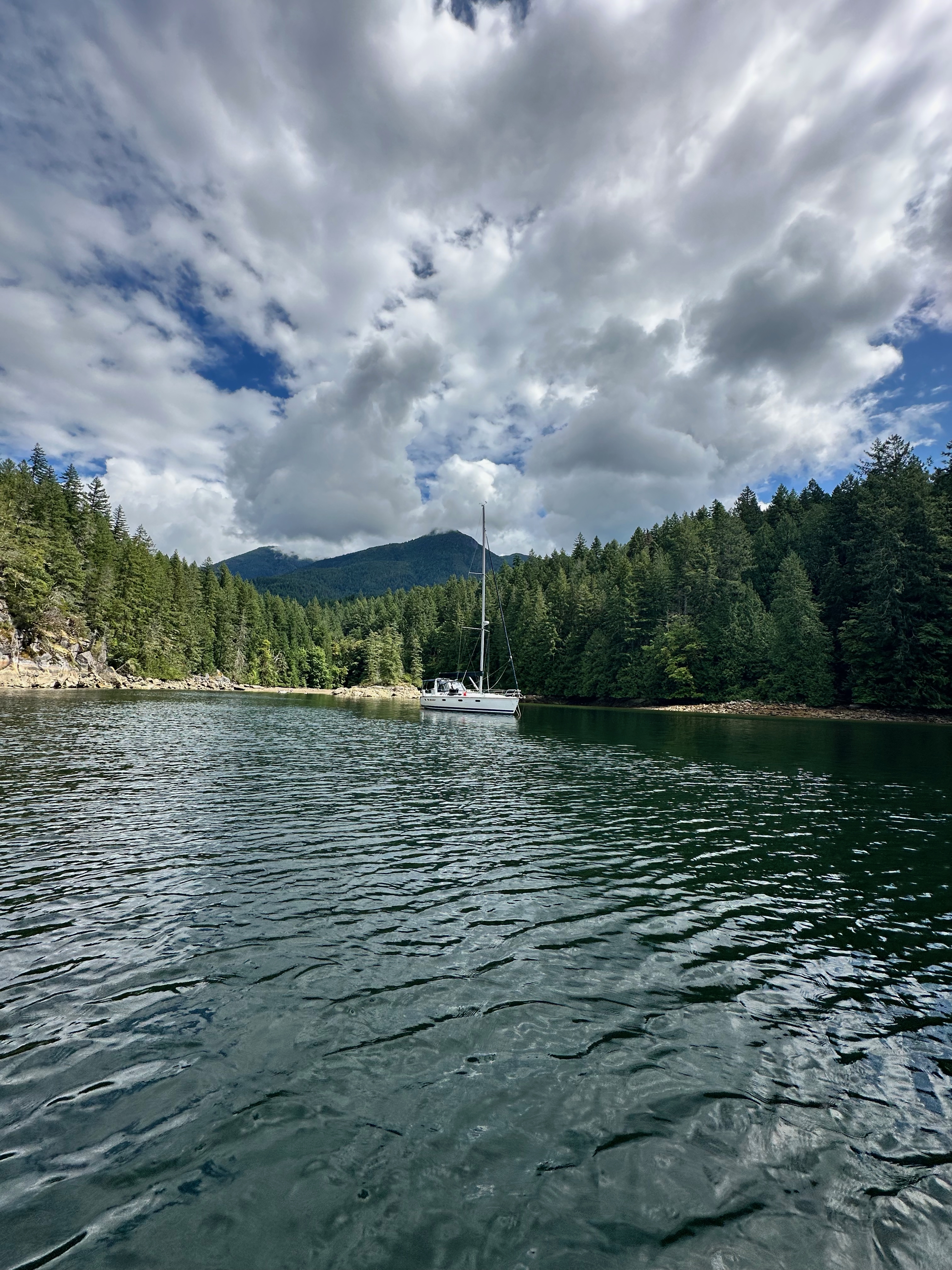 Oceanus anchored beneath dramatic clouds in Melanie Cove
